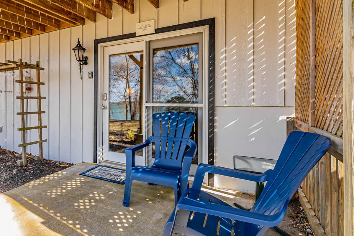An inviting exterior view with two blue chairs positioned outside the front door, a lamp post, and a trellis, surrounded by tranquil landscaping. There is clear, easy access between inside and outside, ideal for letting pets out safely.