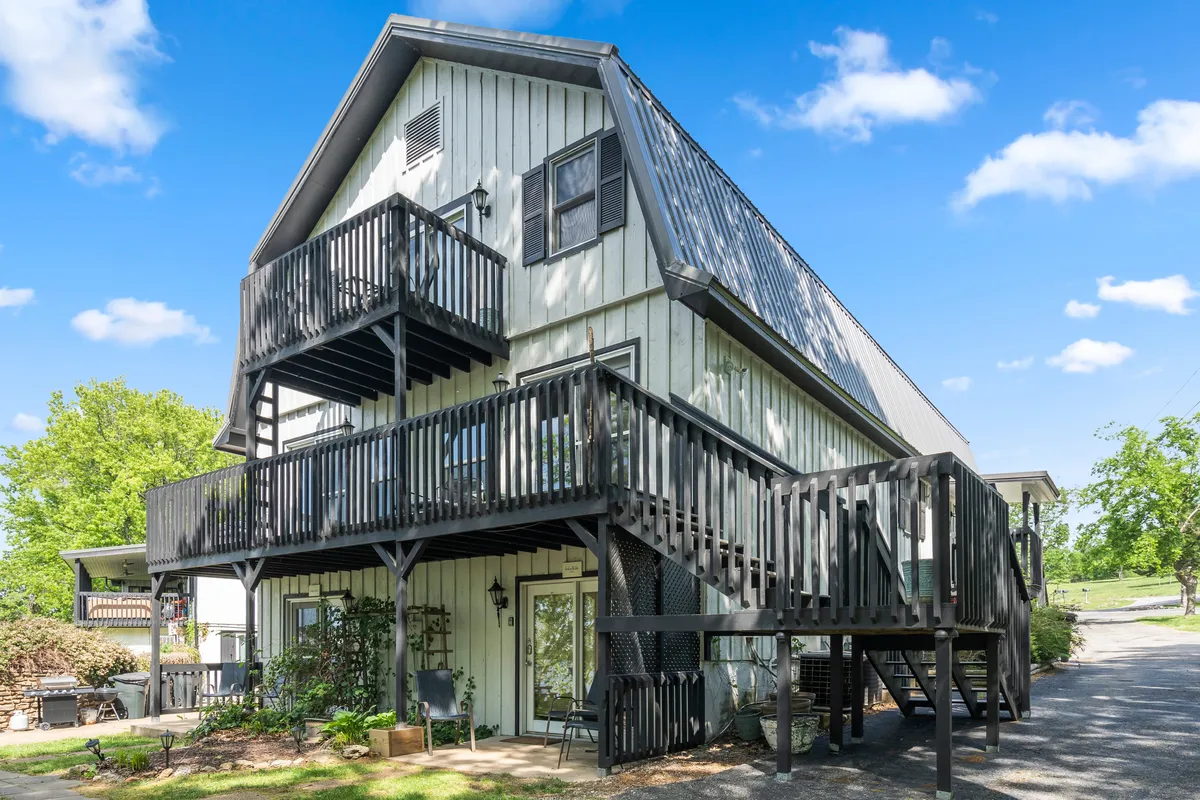 The image captures a multi-level deck attached to a modern lodge, surrounded by lush greenery. The spacious deck is ideal for relaxing, socializing, or enjoying the serene outdoor environment. The architecture blends seamlessly with the natural landscape, highlighting access to the outdoors and offering a welcoming space for guests to unwind after a day of exploring Branson.