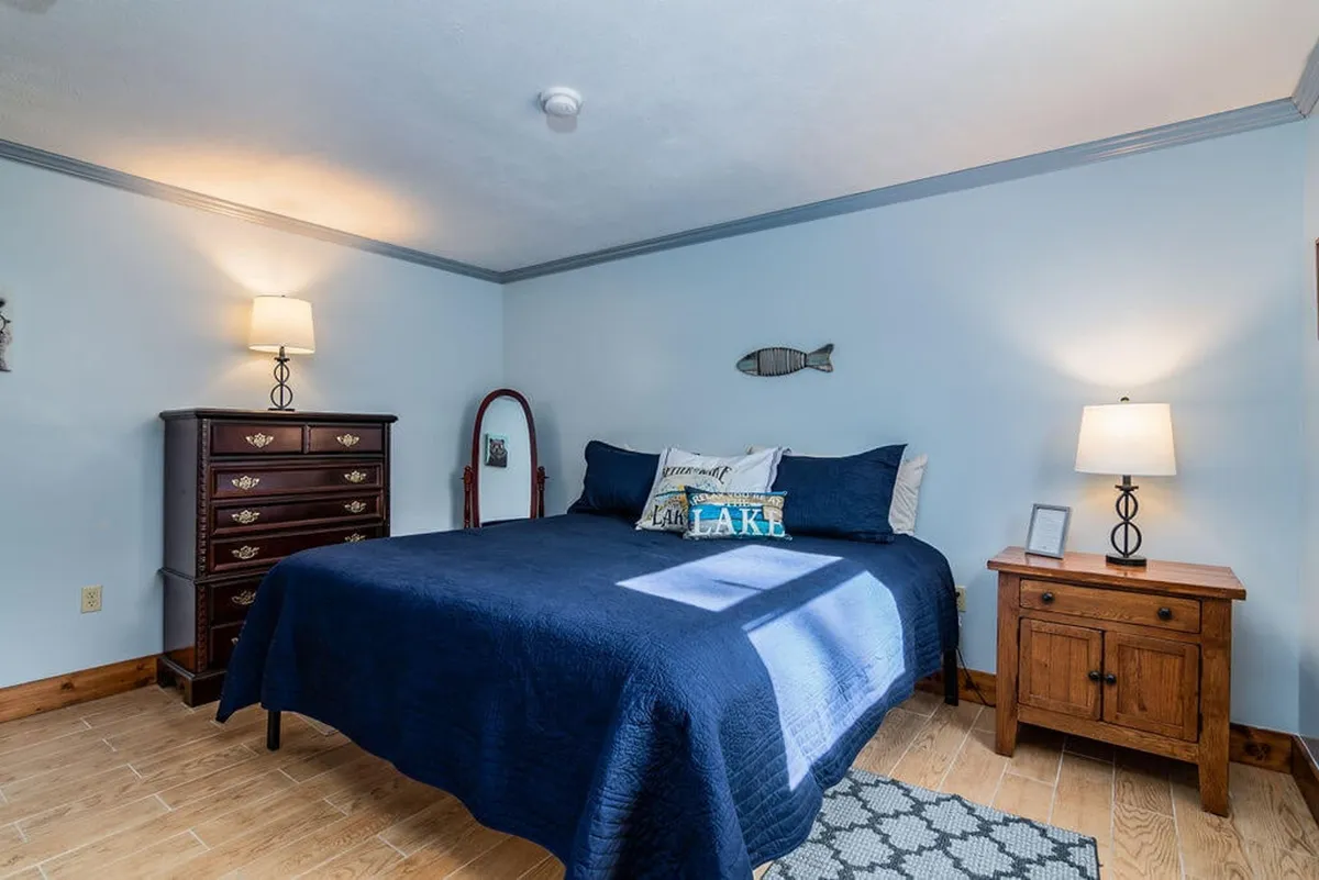 This image features a bed with navy blue bedding, wooden nightstands, decorative fish on the wall, and a lamp emitting a warm glow. The serene, inviting atmosphere is accentuated by soft textures and gentle lighting, with subtle nautical touches that reinforce the section's theme.
