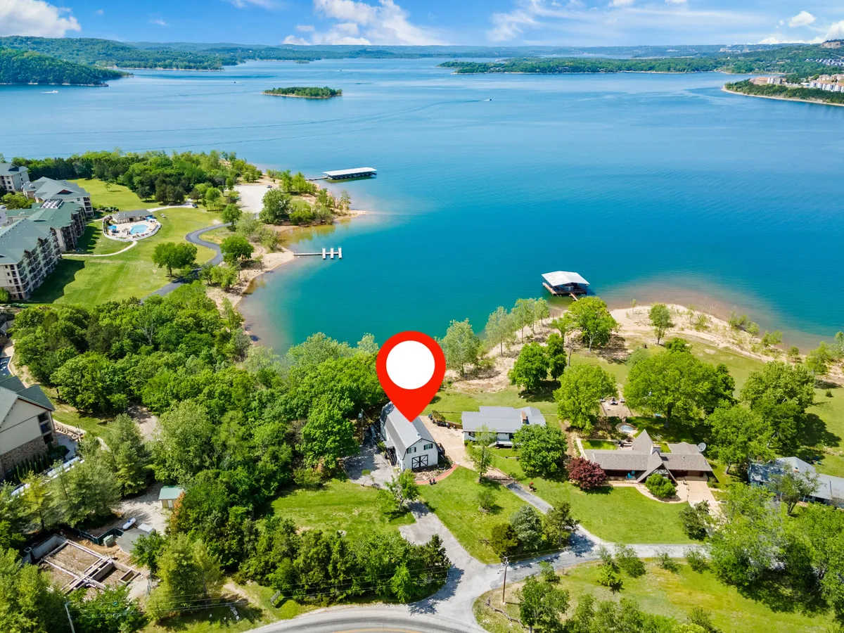 This image captures a scenic lakeside view featuring the lake, the shoreline, the house, and abundant greenery. The tranquil water is perfect for splashing, boating, or fishing, and the inviting porch provides an ideal spot for families to gather and enjoy nature right outside their door.