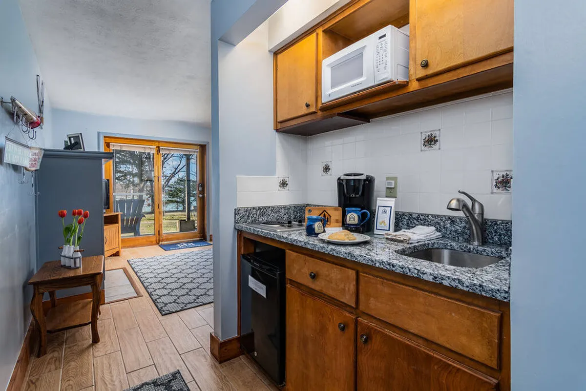A well-equipped kitchenette complete with a coffee maker, snack plates, and a vase of fresh flowers on the counter. Bright natural light fills the space, and there’s a glimpse of the outdoors through a nearby window, creating an inviting spot for meal prep or a morning coffee.
